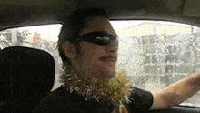 a man wearing sunglasses and a gold tinsel necklace driving a car