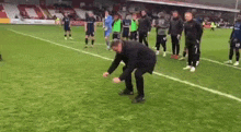 a man is throwing a ball on a soccer field while a group of soccer players are standing around .