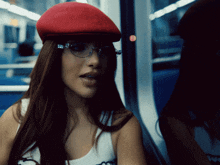 a woman wearing glasses and a red hat is looking out a window