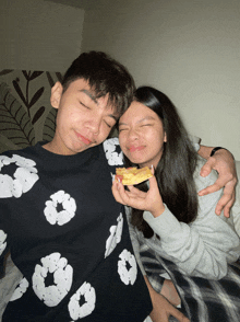 a girl is holding a slice of pizza over a boy 's shoulder