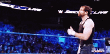 a man in a black tank top is standing in a wrestling ring with the words w live on the screen behind him