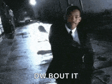 a man in a suit and tie is walking down a wet street at night .