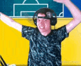 a man wearing headphones is standing with his arms outstretched in front of a soccer field .