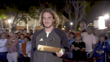 a man in an adidas jacket holds a gold bar