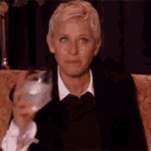 ellen degeneres is sitting on a couch with a glass of wine in her hand .