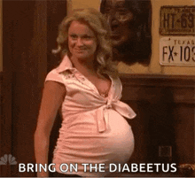 a pregnant woman in a pink shirt is standing in front of a sign that says `` bring on the diabetes '' .