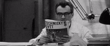 a man wearing glasses is reading a book while sitting at a desk .