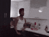 a man wearing a red hat and a white tank top is standing in a kitchen
