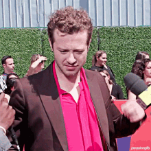 a man wearing a red shirt and a brown suit is being interviewed by a reporter