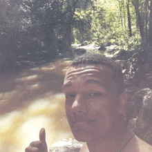a shirtless young man giving a thumbs up in front of a river