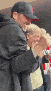 a man wearing a black hat with a red r on it hugs another man
