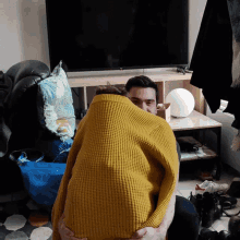 a man in a yellow sweater is hugging another man in front of a tv
