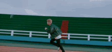 a man in a green jacket is running on a track with the letter f behind him