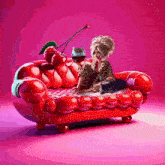 a woman is sitting on a red couch with a cherry on top