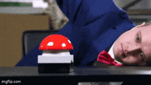 a man in a suit and tie is laying on a table next to a red button .