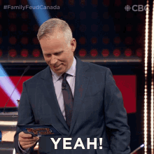 a man in a suit holds a piece of paper that says yeah