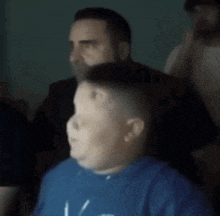 a man in a blue shirt is making a funny face while sitting next to another man .