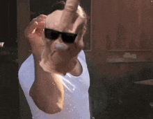 a man wearing sunglasses and a white shirt is giving the middle finger to the camera .