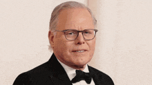 a man in a tuxedo and glasses is standing in front of a wall .