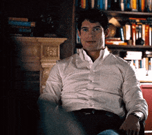 a man in a white shirt is sitting in front of a book shelf