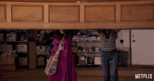 two women carrying a large piece of wood with a netflix logo behind them
