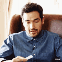 a man in a denim shirt is sitting in a chair looking at a piece of paper