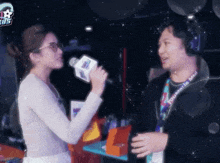 a woman is singing into a microphone while talking to a man with a lanyard around his neck that says councils mall