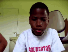 a young boy wearing a souderton shirt looks at the camera