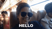 a woman wearing sunglasses says hello while sitting in a chair