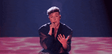 a young man is singing into a microphone while sitting on a stage .