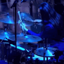 a woman in a blue jacket is playing drums on a stage