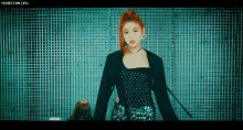 a woman with red hair and a black jacket is standing in front of a grid wall .