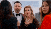 a man in a tuxedo and bow tie stands between two women