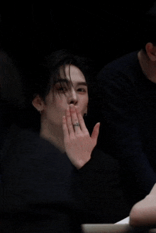 a man with a ring on his finger is sitting in a dark room with his eyes closed