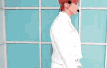 a man with red hair is wearing a white jacket and a microphone while standing in front of a blue wall .