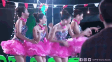 a group of women in pink dresses are dancing in a row .