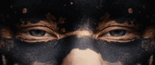 a close up of a person 's eyes with black and gold paint on their face