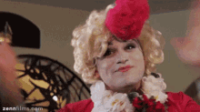 a man in a drag queen costume is wearing a red jacket and a red hat .