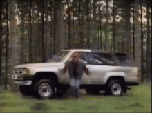 a man is running towards a silver suv in the middle of a forest .