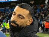 a man with a beard wearing a black jacket with the lfc logo on the bottom