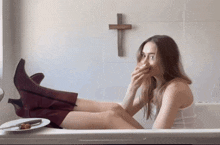 a woman sitting in a bathtub with a cross on the wall