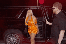 a woman in an orange dress is getting out of a car