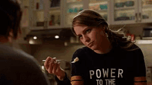 a woman is holding a spoon in her hand and wearing a black shirt that says power to the .