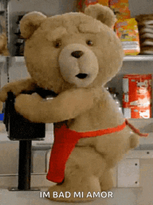 a teddy bear wearing a red apron is standing in front of a sign that says " im bad mi amor "