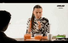 a woman is sitting at a table eating carrots while a man watches .