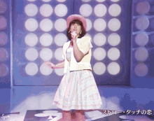 a woman in a pink hat sings into a microphone in front of a wall with circles