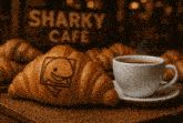 a croissant with a fish on it sits next to a cup of coffee at the sharky cafe