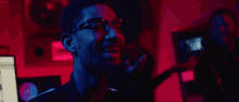 a man wearing glasses is standing in a dark room with a red light behind him .