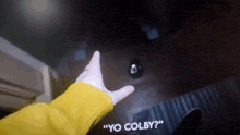 a person wearing a yellow jacket says " yo colby " in a dark room