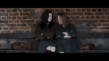 two girls are sitting on a bench with their arms crossed .